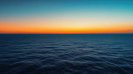 Obraz premium A panoramic view of the open sea at twilight, with the sky transitioning from orange to deep blue and the water calm.