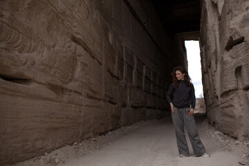 A beautiful woman dressed in gray pants and a sweater walks against the background of a career in stylish clothes