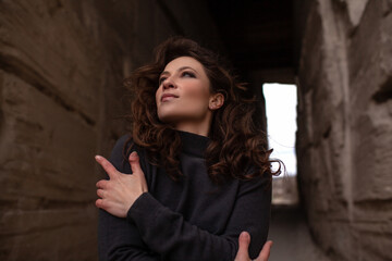 A beautiful woman dressed in gray pants and a sweater walks against the background of a career in stylish clothes