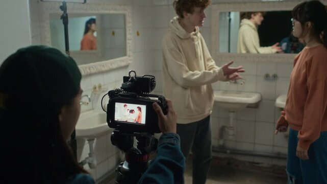 Shot with changing focus of female operator clapping dumb slate and recording video of two actors who playing quarreling scene in washroom. Students filming movie for graduate project