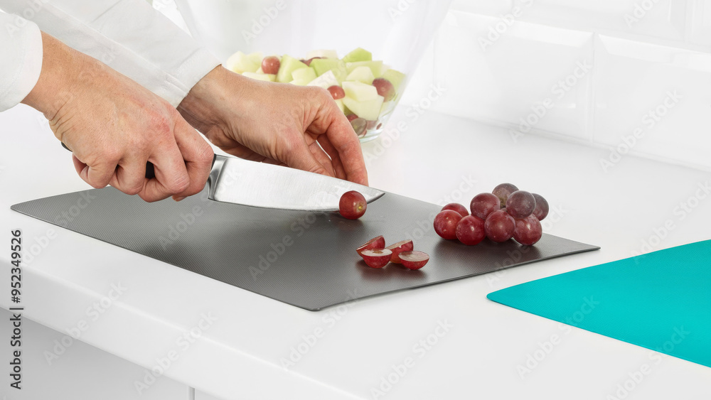 Wall mural Closeup of a person dicing grapes on a plastic cutting surface.