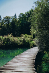 Wooden pathway stretches over vibrant lake in Plitvice Jezera National Park, Croatia. Serene, colorful summer landscape showcases idyllic forest, tranquil waters, lush greenery, natural beauty, and pe