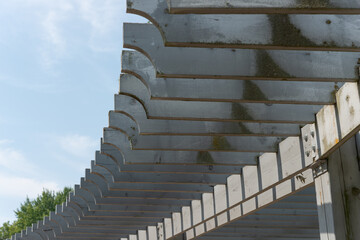 wooden structure, or curved trellis, composed of elegantly cut planks or slats on a blue sky with a dashing smear of cloud