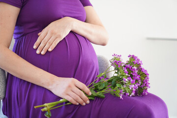 Pregnant woman with flowers holds hands on belly. Motherhood concept. 