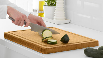 Closeup of a person slicing cucumbers on a wooden cutting board.