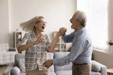 Vivacious elderly 60s spouses holding hands dancing swirling feel happy having fun together at...