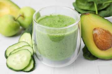 Tasty green smoothie in glass and products on white tiled table, closeup