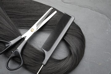 Naklejka premium Black hair strand, comb and professional scissors on grey surface, flat lay