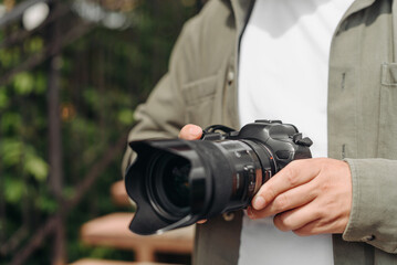 dslr camera in hands, young adult caucasian photographer in white t-shirt at work outdoors in sunny summer day