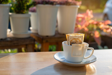 Morning coffee with sunlight and potted plants with drip coffee filters placed on wooden table on garden.