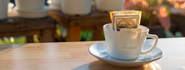 Morning coffee with sunlight and potted plants with drip coffee filters placed on wooden table on garden.