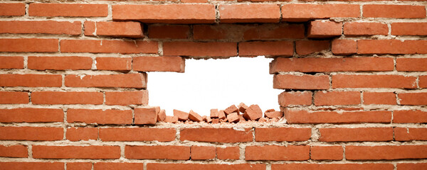 A red brick wall with a hole in it revealing a bright blue sky. The hole is partially filled with loose bricks.