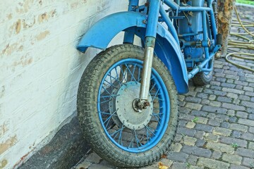 one front old black tire  wheel with spokes fork and wing of blue retro heavy motorcycle stands...