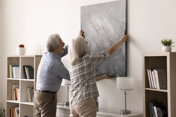 Rearview aged spouses hanging on wall fine-art picture in cozy modern living room, decorating domestic space, changing design with new beautiful stylish artwork. Improve coziness and indoor atmosphere