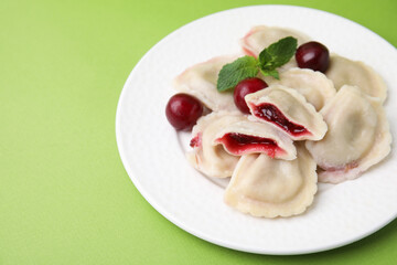 Traditional Ukrainian dumplings (varenyky) with cherries on green background, closeup. Space for text