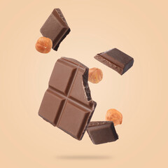 Pieces of tasty chocolate and hazelnuts falling on dark beige background