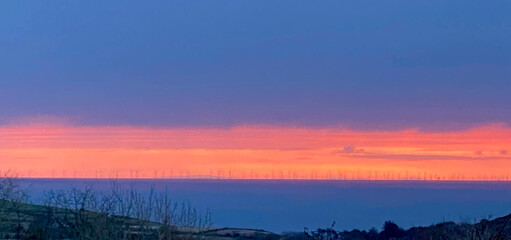 Windmills of a distant wind farm on the English coast seen at sunset over the Irish Sea from the Isle of Man