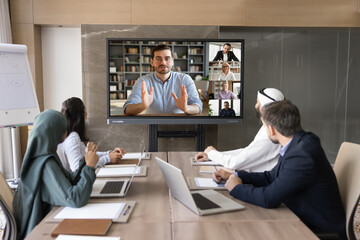 Online business coach giving webinar to multiethnic audience, speaking from large screen to diverse...