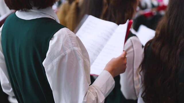 Church choir concert in cathedral, choral artists singing, group of European boys and girls singing in a chorus, students and choristers in white and green uniform performing on stage with conductor