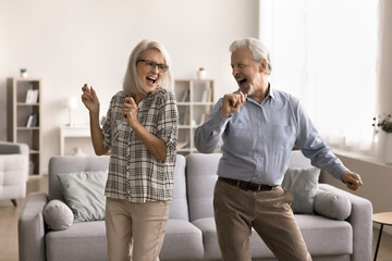 Happy carefree retired 60s couple dancing in cozy living room, enjoy active pastime and hobby,...