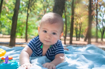 Baby boy lies down on a blanket in the park. Around him are leaves. About 8 months.