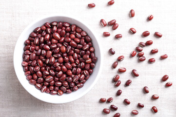 Adzuki beans in a white bowl on linen fabric. Also known as azuki, aduki, red, or red mung bean. Dried seeds of Vigna angularis, a member of the legume family Fabaceae, used in East Asian cuisine.
