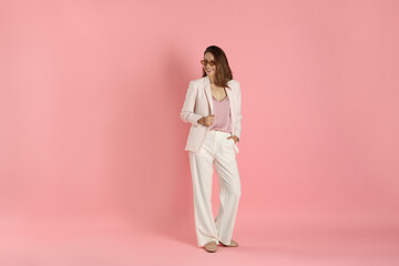 Beautiful woman in stylish white suit and sunglasses on pink background