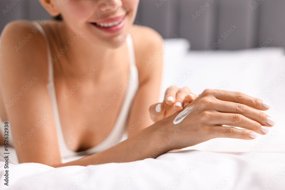 Poster Smiling woman applying cream onto hand on bed, closeup. Body care