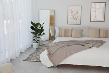 Large bed, houseplant and full-length mirror near window in room. Stylish bedroom interior