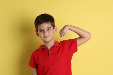 Cute little boy showing his bicep on yellow background