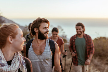 Group of friends smiling while hiking on a mountain trail at sunset