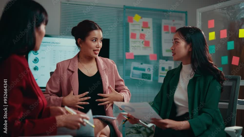 Poster Three businesswomen are having a meeting in the office. They are discussing strategy and using charts and graphs to illustrate their points