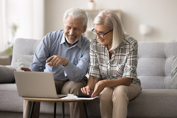Smiling mature couple sit on sofa make budget analysis, use calculator and laptop, discuss expenses...