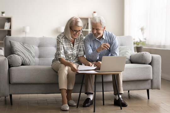 Happy elderly couple sit on couch, read paper letter, sorting out documents, enjoying paperwork, checking investment, reviewing insurance, mortgage or rental agreement with good terms and conditions - Powered by Adobe