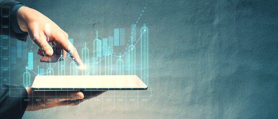 Businessman using a tablet to interact with a holographic financial graph on a concrete background.