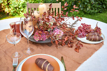 Fall table setting with pumpkins and leaves and hydrangea in brown and burgundy tones