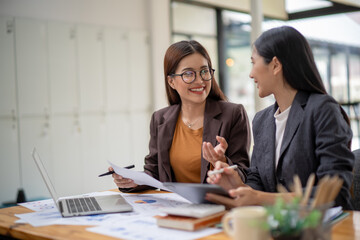 Fototapeta premium Two women in suits are talking at a desk with a laptop and a tablet