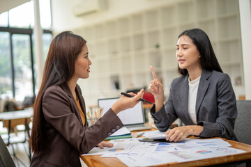 Two women are sitting at a table with papers and a laptop