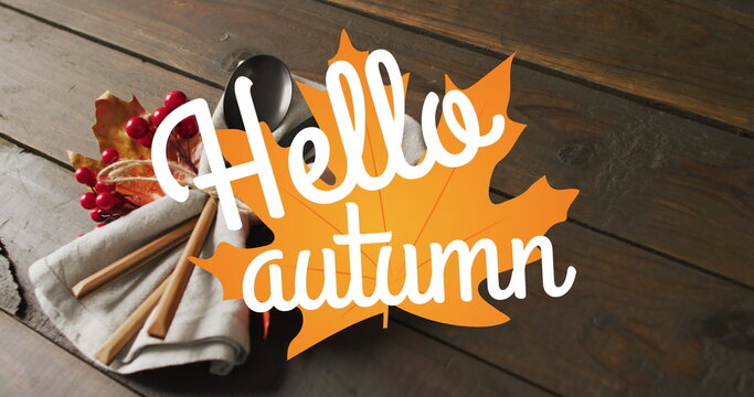 Image of hello autumn text over cutlery and autumn leaves over wooden background