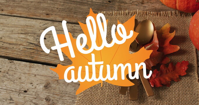Image of hello autumn text over cutlery and autumn leaves over wooden background