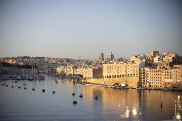 Obraz premium Valletta harbor at sunrise with sparkling sea and historic buildings.