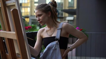 Young artist woman painting on canvas on an easel outdoors.
