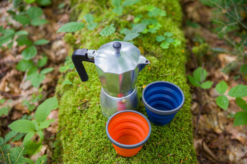 Coffee pot and metal cup on a large stone against the background of a mountain river. Coffee pot on...