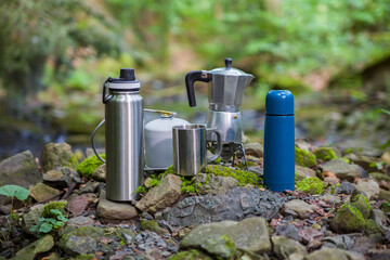 Coffee pot and metal cup on a large stone against the background of a mountain river. Coffee pot on a stone slab against a blurred background of nature.