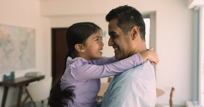 Cheerful loving Indian dad holding adorable little daughter in arms, cuddling child, enjoying fatherhood. Happy daddy and preschool kid girl playing with noses touch, hugging, smiling, laughing