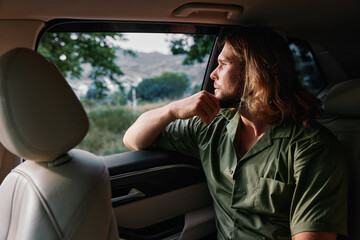 Thoughtful man gazing out of a car window, reflecting on life with a serene landscape in the background