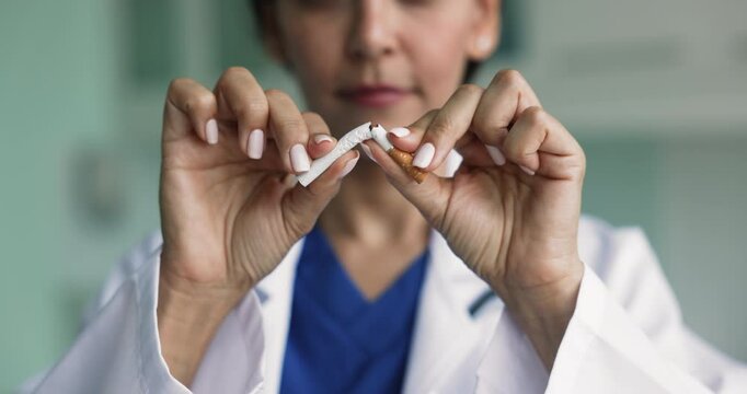 Close up woman doctor breaking cigarette as symbol of smoking cessation, act of quitting smoking, promote healthy lifestyle. Social campaign to help smokers overcome nicotine addiction, improve health