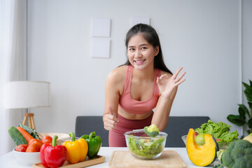 Young fitness woman gesturing ok sign while holding a bowl of fresh salad, promoting healthy lifestyle with organic vegetables