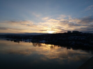 Obraz premium Sunset over the river in a small town. Wide river in the rays of the winter sun. Stunning views of two banks of the river