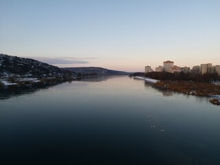 Sunset over the river in a small town. Wide river in the rays of the winter sun. Stunning views of two banks of the river
